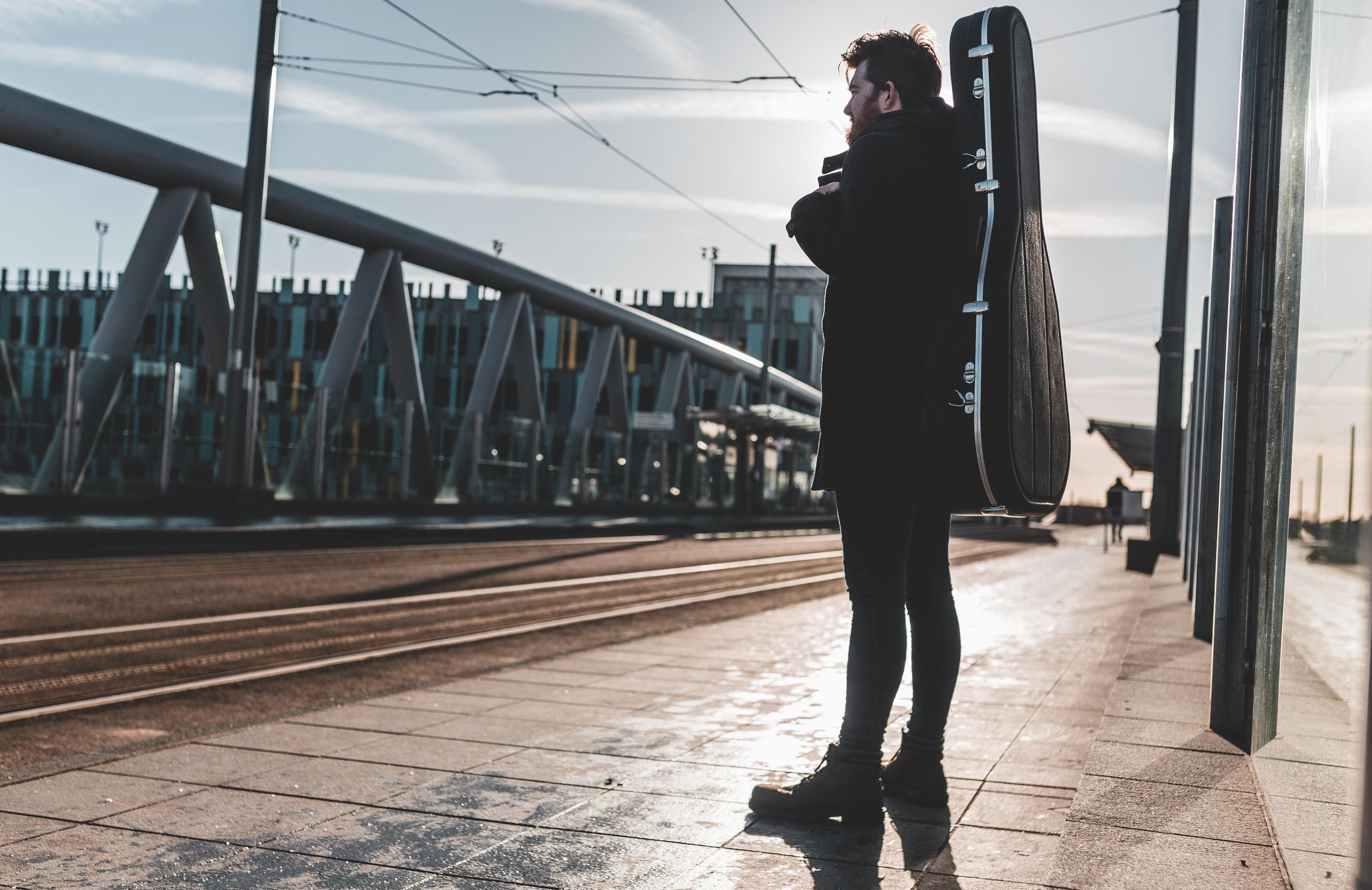Musician carrying a Hiscox guitar case as a backpack at a tram station